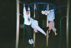 three people are hanging upside down on a playground structure at night, while one person is holding onto the bars