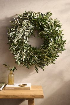 an olive wreath hangs on the wall next to a table with a book and vase