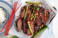 a plate with meat and vegetables on it next to chopsticks, rice and sauce