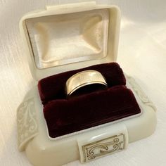 an empty ring box with a gold wedding band in it on a white tablecloth