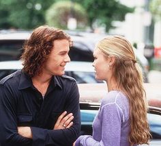 a man and woman standing next to each other in front of a car on the street