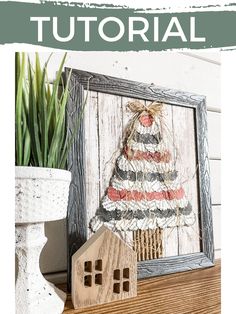 a small wooden house sitting next to a potted plant on a shelf in front of a picture frame