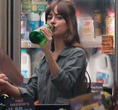 a woman drinking from a green bottle in a grocery store