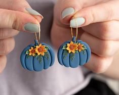 a woman is holding two small pumpkins with sunflowers painted on them, while wearing matching earrings