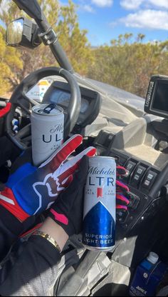 a can of beer sitting on the dashboard of a car next to a gloved hand