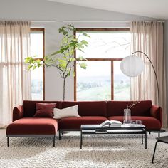 a living room with a red couch, coffee table and large windows in the background