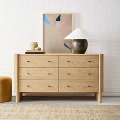 a wooden dresser sitting next to a lamp on top of a rug in front of a white brick wall