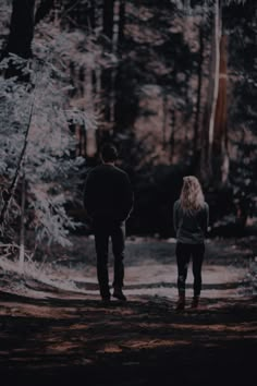 a man and woman walking in the woods at night with their back to each other