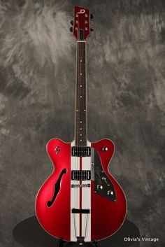 a red and white guitar sitting on top of a black stand in front of a gray background