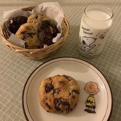 a chocolate chip cookie next to a glass of milk and a basket of cookies on a table