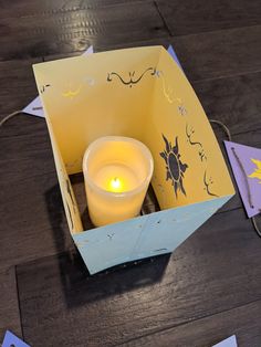 a lit candle in a paper box on a wooden table with cut out pieces of paper