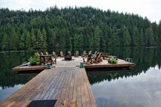 a dock with chairs on it next to the water and trees in the background,