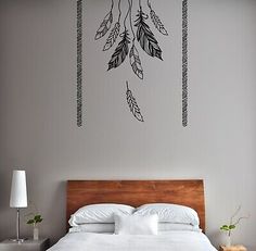 a bed with white sheets and pillows in front of a wall decal that has feathers on it