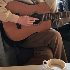 a man sitting down playing a guitar next to a cup of coffee