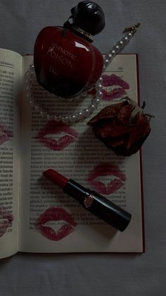 an open book with lipstick, pearls and a bottle of perfume on top of it