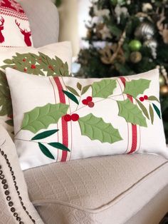 a christmas pillow with holly and mist on it sitting next to a decorated christmas tree