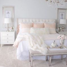 a white bedroom with chandelier, bed and pillows on the top of it