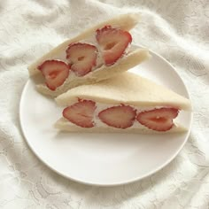 two slices of sandwich with strawberries on it sitting on a plate next to a white lace tablecloth