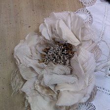 a white flower sitting on top of a table next to a lace covered wall hanging