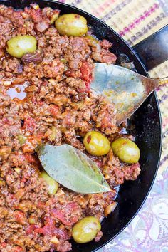 a skillet filled with meat and olives on top of a table