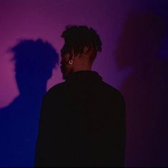 a man standing in front of a purple and blue wall with his shadow on the wall