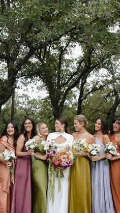 a group of women standing next to each other in front of trees and grass with bouquets