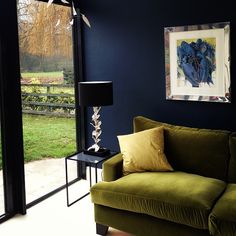 a green couch sitting in front of a window next to a table with a lamp on it