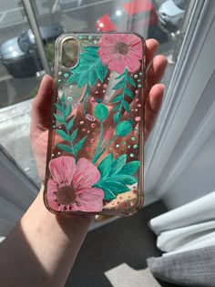 a person holding up a phone case with flowers on it in front of a window