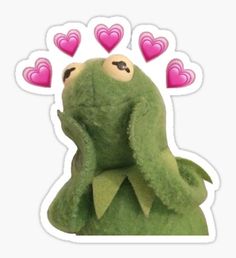 a green stuffed animal with hearts on its head and eyes, sitting in front of a white background