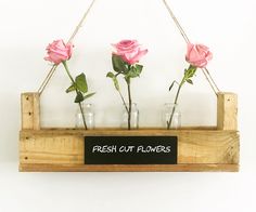 three glass vases with pink roses in them hanging from a wooden frame that says fresh cut flowers