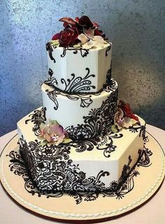 a three tiered wedding cake with black and white designs on the top, decorated with red flowers