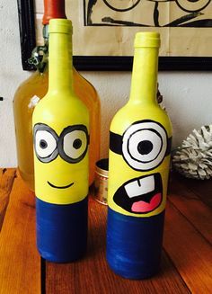 two wine bottles with faces painted on them sitting on a table next to a vase