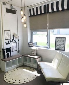 a living room filled with furniture next to a window covered in roman shades and hanging lights