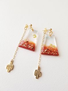 two pieces of glass with gold chains hanging from them on a white surface, one is shaped like a desert and the other has a cactus