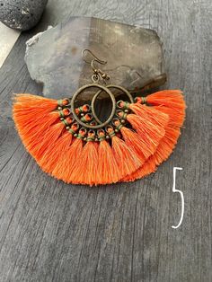 Unique fun colorful and powerful tassel earrings. Made in fan shapes with the red/orange tones. You can choose between 5 different pairs. 3 of them are made with a round plastic base which from where tassels hang and are hold with some brass beads and wax cord. 2 of them are made with a brass wire spiral shape from where the tassels hang with wax cord holding the tassels. Each pair is unique and fun. They are all super light and easy to wear. The earrings with the round piece in the middle are 6 Bohemian Orange Tassel Earrings, Orange Fringe Tassel Earrings For Summer, Adjustable Bohemian Tassel Earrings With Latkans, Bohemian Orange Tassel Earrings For Festivals, Adjustable Orange Tassel Earrings, Adjustable Beaded Tassel Earrings, Beach Drop Tassel Earrings With Latkans, Beach Drop Earrings With Tassel Latkans, Traditional Fringe Earrings