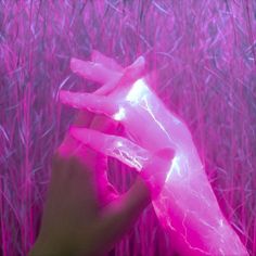 a hand is holding something pink in front of some tall grass and purple light from the camera