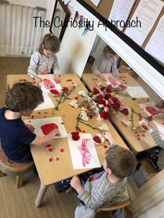 three children are sitting at a table making paper flowers with red and white paint on them