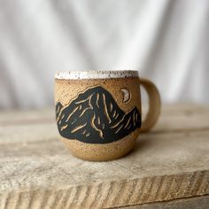 a coffee cup sitting on top of a wooden table next to a white wall with a mountain scene painted on it