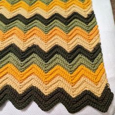 a crocheted blanket is laying on top of a white tablecloth with an orange, green, yellow and black zigzag pattern