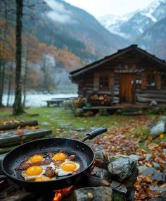 two fried eggs in a frying pan on top of a campfire next to a cabin