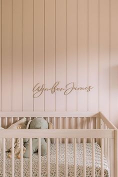 a baby crib with a stuffed animal in it and name on the wall above