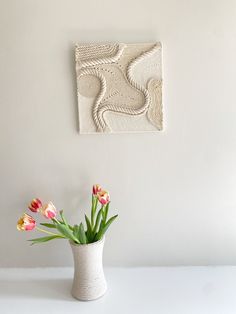 a vase with some flowers in it next to a white wall and a painting on the wall