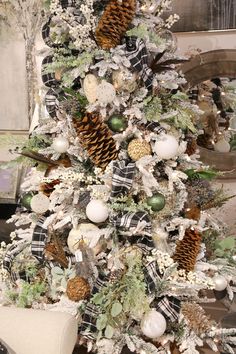 a white christmas tree decorated with plaid and pine cones