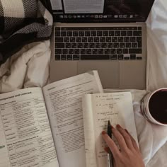 a woman is writing in her notebook next to an open book and a laptop computer