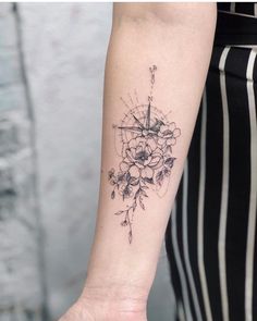 a woman's arm with a compass and flowers tattoo on the left inner forearm