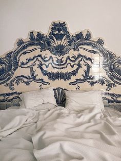 an ornate headboard with white sheets and pillows on a bed in front of a wall