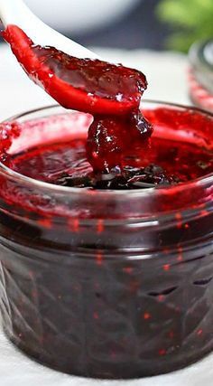 a spoon full of jam on top of a glass jar filled with red fruit preserves