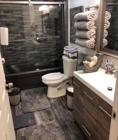 a bathroom with gray tile and wooden cabinets, toilet, sink, and shower stall