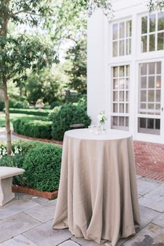 a table with a cloth draped over it in front of a white building and trees