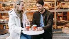 a man and woman sitting at a table with coffee cups in front of their faces